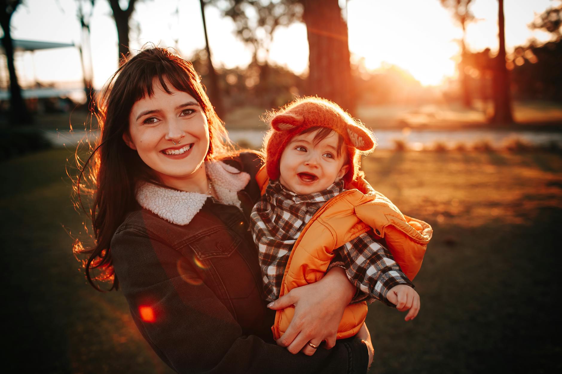 Mama trzymająca uśmiechnięte dziecko w parku o zachodzie słońca